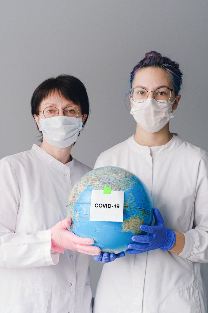 Two healthcare professionals in masks and gloves holding a globe with a COVID-19 label.